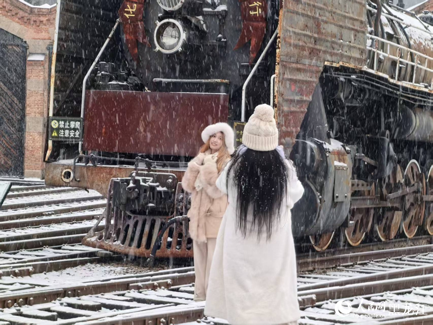 游客在雪中与机车合影留念。